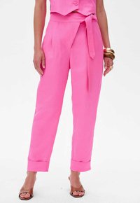 Roze linnen broek met hoge taille, een strikceintuur, zijzakken en opgerolde manchetten. De soepele textuur en de getailleerde pasvorm verbeteren het ontwerp.