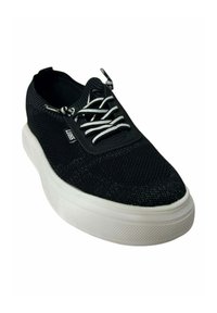 Zapatilla de tela negra con cordones blancos, parte superior texturizada, suela de goma blanca y punta redondeada. Incluye una etiqueta de logo en el lateral.