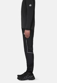 Zwarte fleece met lange mouwen en zwarte broek met reflecterende accenten. Schoeisel heeft textuur gripzolen en een vetersluiting.