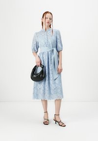 Lyseblå blonde midi-kjole med pufferm og knapperekke foran. Kombinert med en svart veske og svarte hæler med stropper, som fremhever en midjevekt.