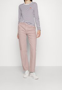 Randig långärmad topp i vitt och lila, kombinerad med ljusrosa cargobyxor med sidofickor, och vita sneakers med mjuka detaljer.