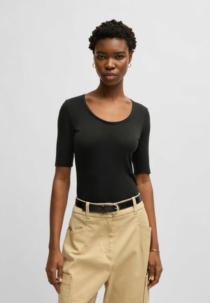 Zwarte geribbelde bodysuit met korte mouwen en een ronde halslijn, gecombineerd met beige broek en een zwarte riem met een gouden gesp.