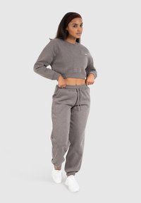 Grijze cropped sweatshirt met lange mouwen en ronde hals, gecombineerd met grijze joggingbroek met elastische boorden en een trekkoord in de taille. Witte sneakers.