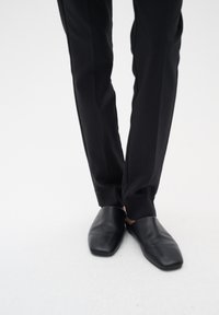 Černé kožené slip-on boty se čtvercovou špičkou, doplněné o upravené černé kalhoty. Boty mají hladký povrch a minimalistický design.