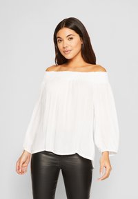 Witte off-shoulder blouse met een smock-halslijn, lange luchtige mouwen en een losse pasvorm, gemaakt van lichte, gestructureerde stof.