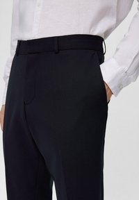 Marineblauwe op maat gemaakte broek met een soepele textuur, voorzien van een platte voorkant, riemlussen en zijzakken, gecombineerd met een witte knoopsluiting blouse.