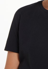Černé bavlněné tričko s krátkými rukávy, kulatým výstřihem a bezešvou konstrukcí ramen. Hladká textura, jednobarevné, bez vzorů nebo akcentů.
