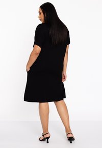 Zwart kortekleding met een ontspannen vorm, gemaakt van zachte stof, met zijzakken en een lengte tot halverwege de kuit. Gecombineerd met zwarte hoge hakken sandaal.