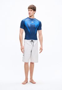 Ανδρικό κοντομάνικο rash guard σε σκούρο μπλε με ανοιχτότερα μπλε στοιχεία· συνοδεύεται από ανοιχτό γκρι μαγιό με κορδόνι στη μέση και πλαϊνή τσέπη.