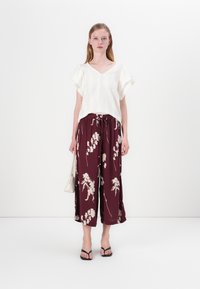 Hvit strukturert strikket topp med korte ermer, kombinert med burgunder blomstermønstrede vide bukser. Svarte flip-flops og en liten sølvveske.