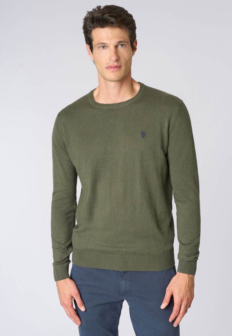 Maglione a maglia verde oliva con maniche lunghe e scollatura a girocollo. Presenta polsini e orlo a coste, con un piccolo logo ricamato sul petto.