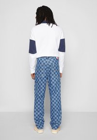 Bílá mikina s námořnickými rukávy, kombinovaná s modrými kostičkovanými džíny cargo, které mají více kapes a logo štítek na zadní straně.