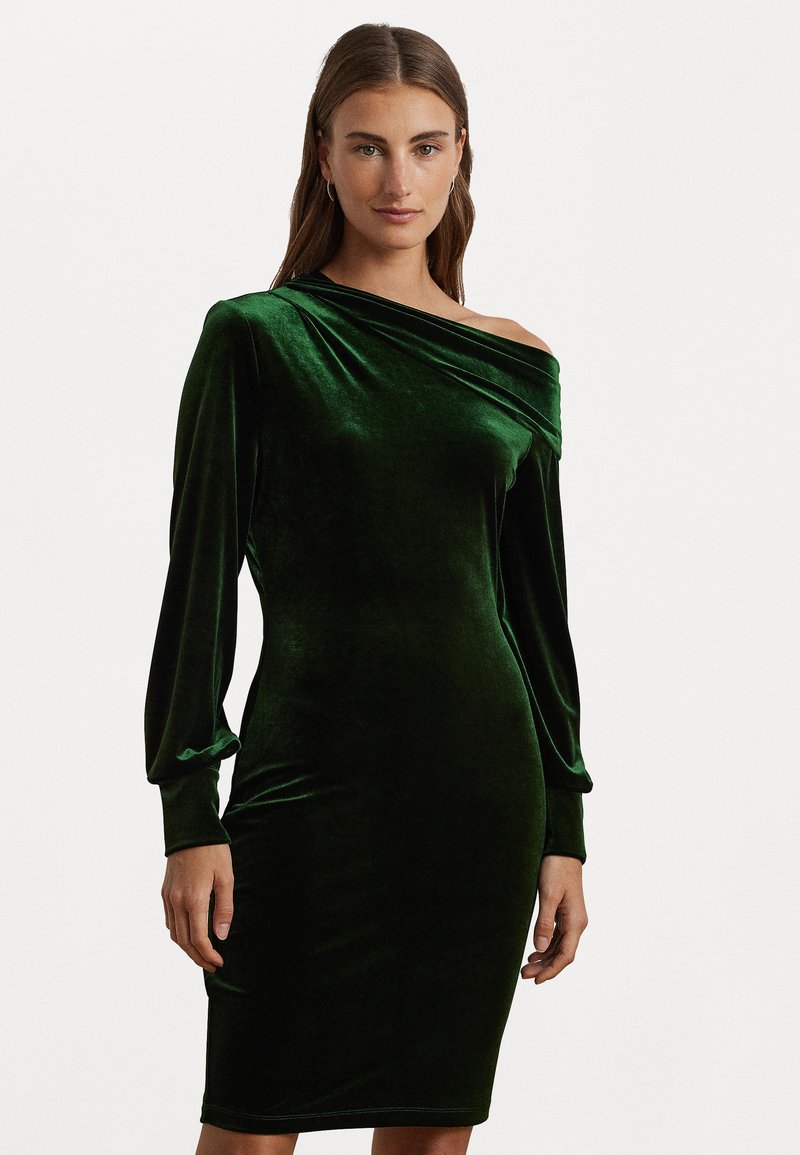 Μακρύ μανίκι πράσινο φόρεμα από βελούδο, με ένα ώμο και ντραπαρισμένο ντεκολτέ. Εφαρμοστό σιλουέτα, μέχρι το γόνατο με λεία υφή.