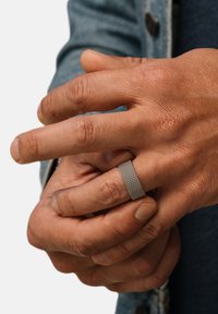 Struktureret sølv ring båret på en hånd med naturlig hudfarve, prydet med en glat overflade og et subtilt netmønster, foran en denim baggrund.
