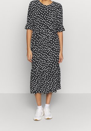 Abito nero a fiori con margherite bianche, maniche corte con volant e orlo a strati, abbinato a sneaker bianche. Tessuto di cotone, design fino al ginocchio.