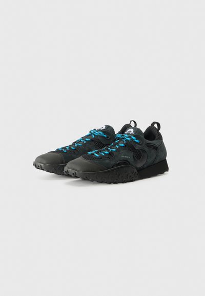 Black athletic shoes with a textured finish, featuring bright blue laces, mesh panels, and a rugged outsole with circular patterns.