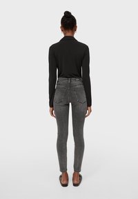 Camisa negra de manga larga combinada con jeans ajustados de color gris oscuro. Los jeans tienen dos bolsillos en la parte trasera y un diseño de cintura alta.