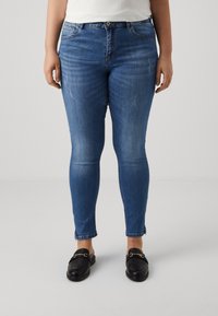 Blå denimjeans med slim fit, med subtil slitning, standard femficksdesign och en enkel fåll, tillsammans med svarta slip-on skor.