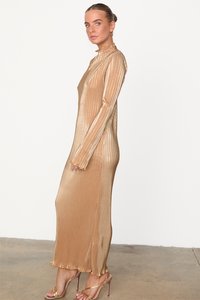 Robe longue et ajustée en tissu ribbé métallisé doré, avec des manches longues et un col haut. Elle présente une fente à l'ourlet et est accompagnée de talons à lanières.