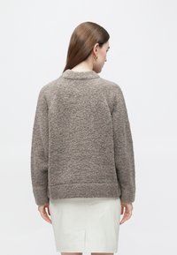 Brun, texturerad tröja med rund hals och långa ärmar, med en något kortare fåll. Kombinerad med en ljusfärgad kjol.