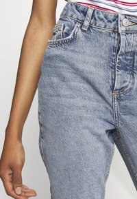 Džíny s vysokým pasem v modré barvě s vybledlým efektem, pěti kapsami, kontrastním šitím a kovovým zapínáním na pasu.