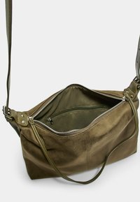 Borsa a tracolla in suede verde oliva con chiusura a zip, tracolla regolabile e tasca interna. Texture liscia con dettagli cuciti.