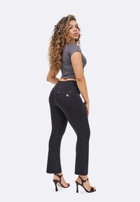 Mustat farkut, joissa on tiukka muotoilu ja lievä lievitys lahkeissa, yhdistettynä harmaaseen ribattu crop-toppiin ja mustiin korkokenkiin.