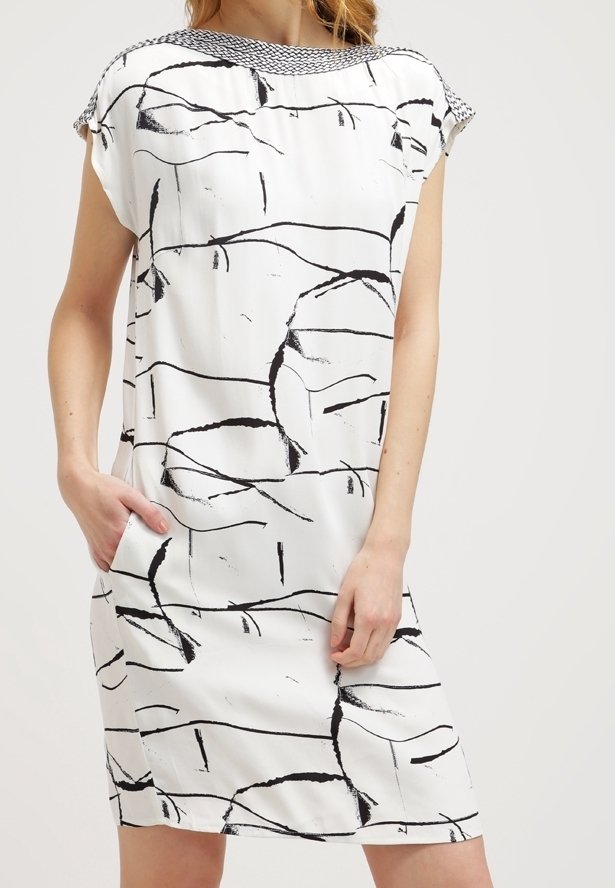 Abito bianco con linee astratte nere, maniche corte e un colletto testurizzato bianco e nero. Presenta tasche laterali e una linea dritta.