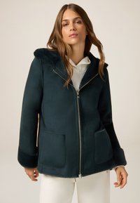 Chaqueta verde oscuro con cremallera y capucha de piel sintética, con puños también de piel sintética, que presenta dos bolsillos frontales y un acabado suave. Diseñada con un corte relajado.