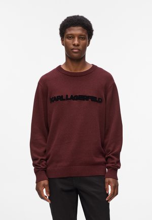 Mørkerød strikket sweater med rund hals, der har et sort "KARL LAGERFELD" logo på tværs af brystet. Løs pasform med ribstrikkede manchetter og kant.