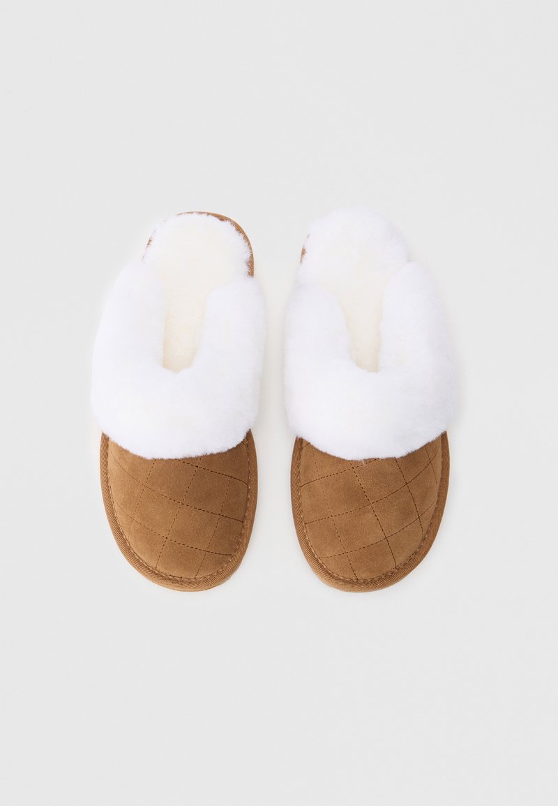Braune Wildlederhausschuhe mit weißem Kunstfellfutter. Gestepptes Design im Zehenbereich. Offenes Rücken-Design für einfaches Anziehen. Weiche, gemütliche Optik.