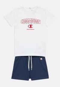 Λευκό βαμβακερό T-shirt με κόκκινο γραφικό "Champion", σε συνδυασμό με σκούρα μπλε σορτς που διαθέτουν λογότυπο και κορδόνι, και τα δύο casual και ελαφριά.