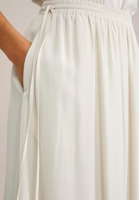 Gonna maxi di un leggero avorio con cintura elastica, tasche laterali e una texture di tessuto liscia e fluida. Cordonetto regolabile in vita.