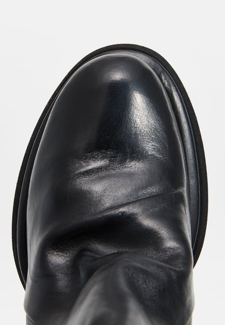 Czarne skórzane buty z okrągłym noskiem i subtelnym połyskiem, charakteryzujące się gładką powierzchnią i lekko podwyższoną podeszwą. Czysty design bez widocznych akcentów.