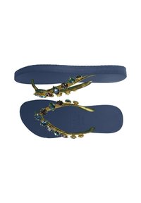 Tongs en caoutchouc bleues avec une sangle dorée ornée d'accents de pierres précieuses colorées et une semelle intérieure texturée. Semelle plate sans soutien de la voûte plantaire.