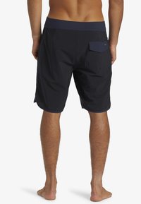 Shorts de bain marine en tissu léger, avec un design uni, une poche arrière et une taille élastique avec des accents contrastants subtils.