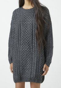 Robe pull en laine grise foncée avec un motif texturé, des poignets côtelés et un col rond, offrant une coupe oversize et un ourlet droit.