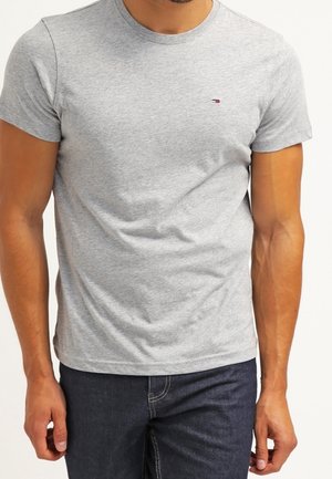 Graues Baumwoll-T-Shirt mit Rundhalsausschnitt, kurzen Ärmeln und einem kleinen Logo auf der Brust, kombiniert mit dunkler Jeans.