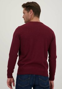 Maroon gebreide trui met lange mouwen, ronde hals en geribbelde manchetten. G gedragen met donkerblauwe jeans, met een eenvoudige achterkant.