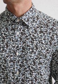 Kragenhemd mit einem weißen und schwarzen Blättermuster sowie blauen Akzenten, aus einem Stoff mit leicht strukturiertem Finish und Knopfdetails.