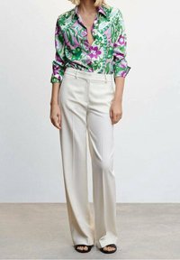 Chemise à manches longues à motif floral vert et rose, associée à un pantalon large à taille haute de couleur crème et des sandales noires à bout ouvert.