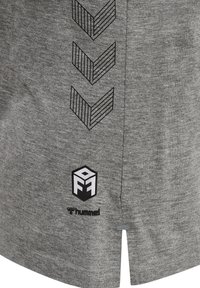 Grå idrottströja med korta ärmar, med svarta chevronränder och en vit logotyp i det nedre hörnet. Mjuk tygtextur.