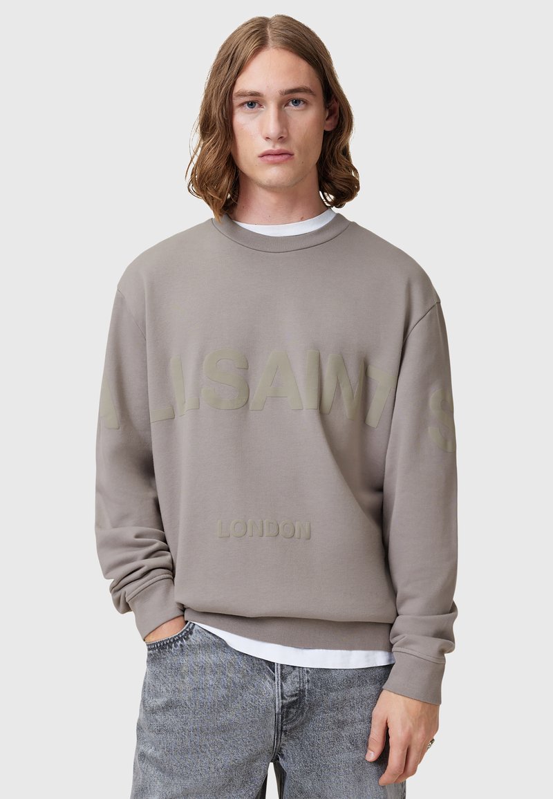 Sweatshirt grigio con testo in rilievo "ALLSAINTS LONDON", scollatura a girocollo, vestibilità rilassata e tessuto morbido. Indossato sopra una camicia bianca.