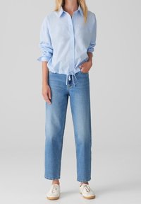 Lyseblå skjorte med knapper og snøre i kanten, kombineret med lyseblå jeans med lige ben og hvide sneakers. Simpelt design og afslappet pasform.