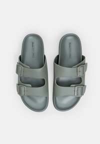 Două sandale din cauciuc de culoare verde măsliniu, cu două catarame reglabile, design cu degetele expuse și o finisare mată. Logo imprimat pe talpa interioară.