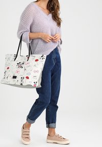 Sac fourre-tout blanc avec des graphismes colorés représentant Mickey Mouse, des monuments parisiens et des cœurs. Pull en tricot lavande doux, jean bleu avec revers roulés, baskets beige.
