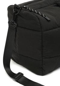 Borsa nera imbottita con texture trapuntata, una cerniera liscia e una tracolla staccabile per un trasporto versatile.