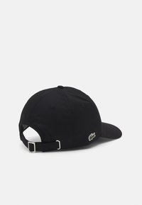 Casquette de baseball noire avec une visière courbée, fabriquée en tissu doux. Présente un logo brodé vert sur le côté et une sangle en métal ajustable.
