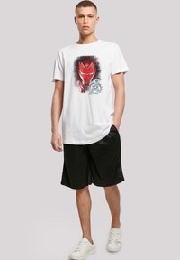 Hvitt bomull T-skjorte med grafikk av et rødt Iron Man-hjelm, paret med svarte shorts og hvite joggesko. Enkel design med avslappet passform.