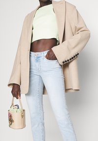 Beiger oversized Blazer, hellgrüner Ripp-Crop-Top, hellblaue High-Waist-Jeans und eine kleine beigetöne Handtasche mit floralen Design.